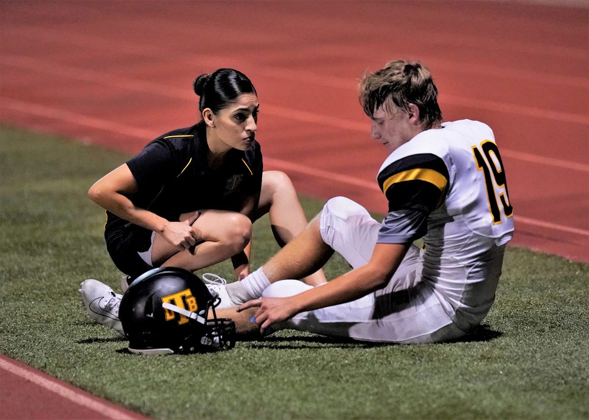 Dr. Jimenez assessing an injured football player's ankle on the sideline